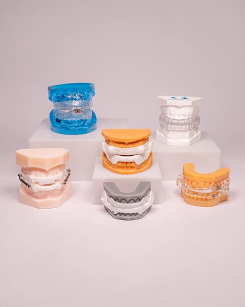 Six oral appliances mounted on upper and lower dental models, displayed on white risers